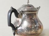 a silver tea pot with a handle on a table