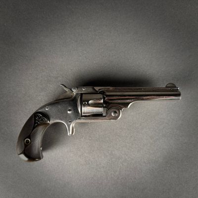 un gros plan d'un revolver posé sur une table, sur fond gris