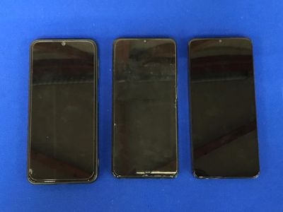 trois iPhones noirs posés côte à côte sur une surface bleue