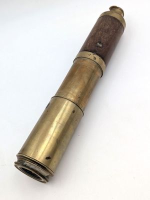 un vieux télescope en laiton muni d'une poignée en bois, posé sur une surface blanche