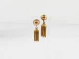 une paire de boucles d'oreilles en or ornées de pompons, présentées sur un support transparent