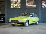une voiture verte garée dans un garage, près d'un mur orné de tableaux