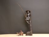 statue représentant un homme assis sur un arbre, accompagné d'un chien et d'un poisson