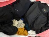 a bag of clothes sitting on a bed next to a pair of shoes