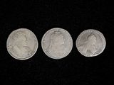 three silver coins sitting side by side on a black surface