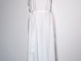 La robe blanche est posée sur un mannequin adossé à un mur blanc.