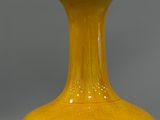 a yellow vase sitting on a table with a gray background
