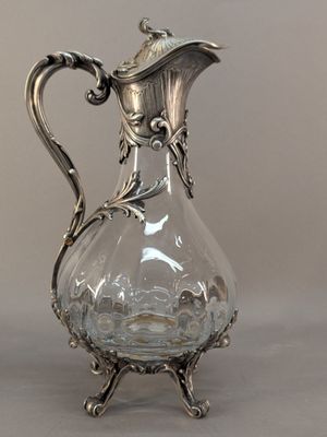 a glass pitcher with a metal handle on a table