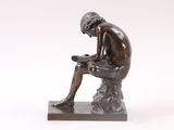 statue of a man sitting on a rock reading a book