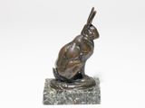 une statue en bronze représentant un lapin assis sur un socle en marbre