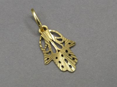 un gros plan d'un pendentif en feuille d'or posé sur une surface grise