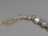 un gros plan sur un collier en argent orné de perles et d'un pompon