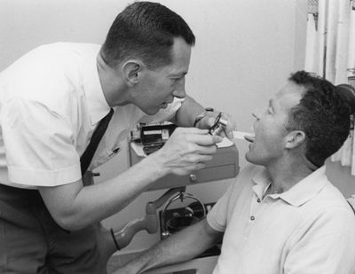 photographie en noir et blanc d'un homme en train de se faire brosser les dents par un dentiste