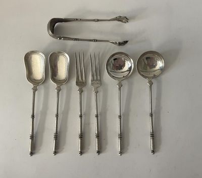 six cuillères et une fourchette sont disposées sur une surface blanche