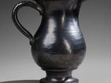 a silver pitcher sitting on a table with a shadow on the floor