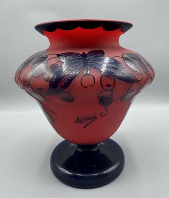 un vase rouge avec un socle noir et orné d'un motif de papillon