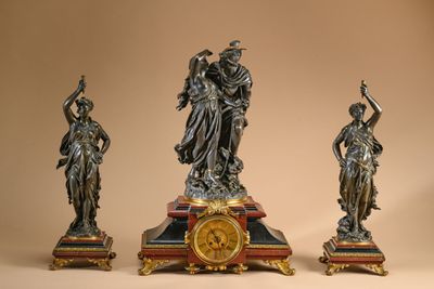 three statues of women with a clock on top of a table