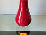 un vase rouge posé sur une table en verre, avec une étiquette jaune