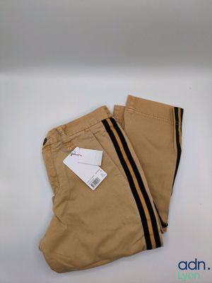 Le pantalon est de couleur beige avec des rayures noires et une étiquette.