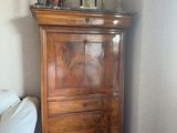 une commode dans un coin d'une chambre où se trouve un lit blanc