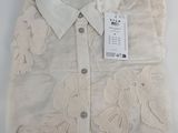 Le t-shirt est blanc, orné de fleurs, et comporte une étiquette.