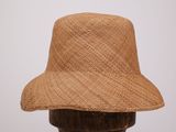 un chapeau de paille marron posé sur un support en bois, adossé à un mur blanc