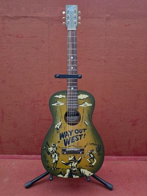 Une vieille guitare est posée sur un support sur lequel est accrochée une pancarte.