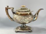 a silver tea pot on a stand with a gold lid