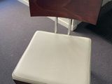 the back of a wooden chair with a white seat sits in front of a window