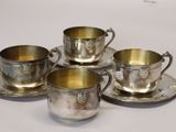 four silver cups and saucers sitting on top of a white table