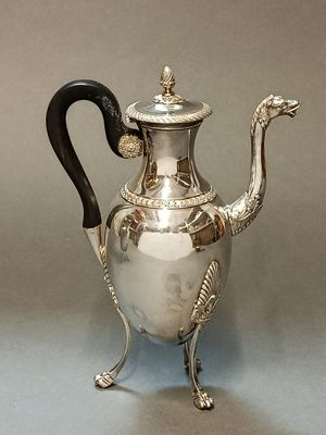 une théière en argent avec une anse noire, posée sur un socle