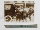a black and white photo of a group of men standing in front of a car