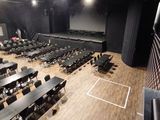 de nombreuses tables et chaises dans une grande salle équipée d'un écran de projection