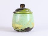 a green jar with a wooden lid on a white surface