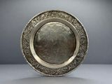 une assiette ancienne en argent, ornée d'un motif floral sur le bord