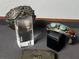 un verre d'eau, un étui en argent et un caillou posés sur une table