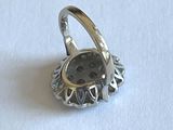 une bague en argent ornée d'un bouton, posée sur une surface blanche