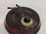 une petite horloge posée sur un socle en bois, sur une surface blanche