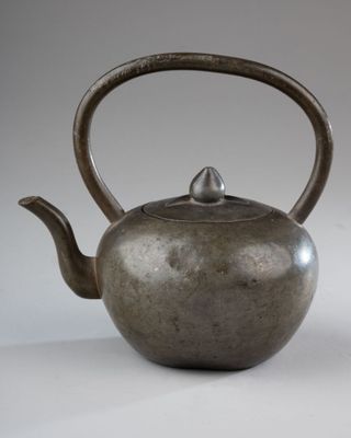 a silver teapot with a handle on a white surface