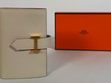 une photo d'un portefeuille blanc orné d'une boucle dorée et d'une boîte orange