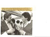 two men standing next to each other holding wine glasses