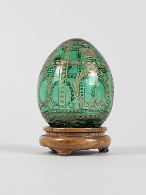 un œuf en verre vert posé sur un socle en bois, sur une surface blanche