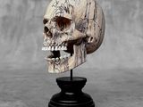 a wooden skull on a black stand with a gray background