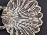 a silver plate with a shell shaped handle on a black surface