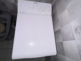 une machine à laver blanche posée dans une salle de bains, à côté des toilettes