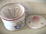 une tasse blanche avec un couvercle rose à côté d'une passoire