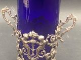 a blue glass vase with a silver base on a table