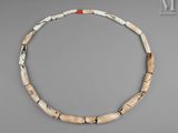 un collier composé de perles en os, avec une perle rouge et blanche