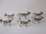 six silver cow shaped dishes on a white surface