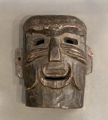 un masque en bois accroché au mur, sur lequel se dessine un sourire